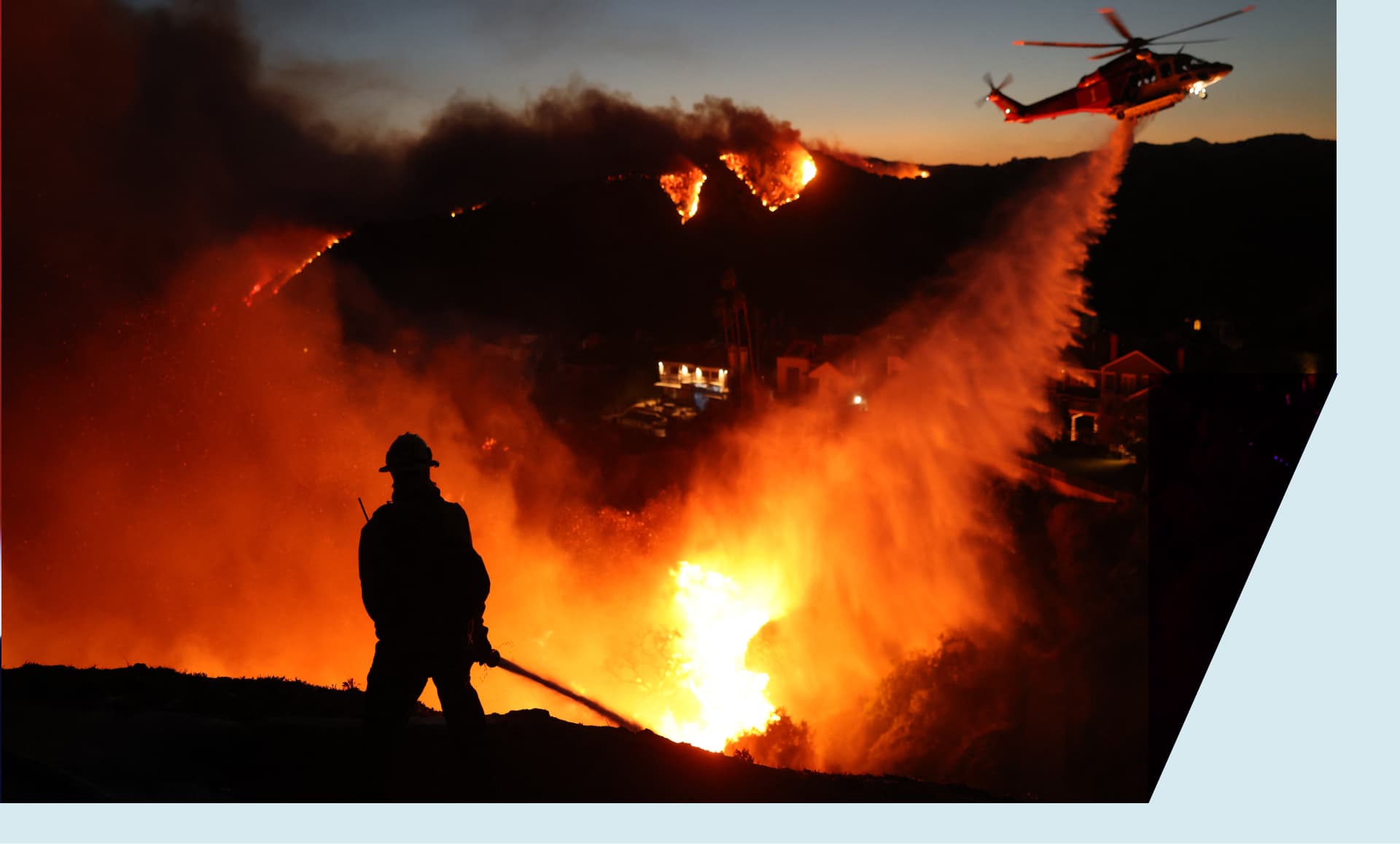 Fire personnel respond to homes destroyed while a helicopter drops water as the Palisades Fire grows